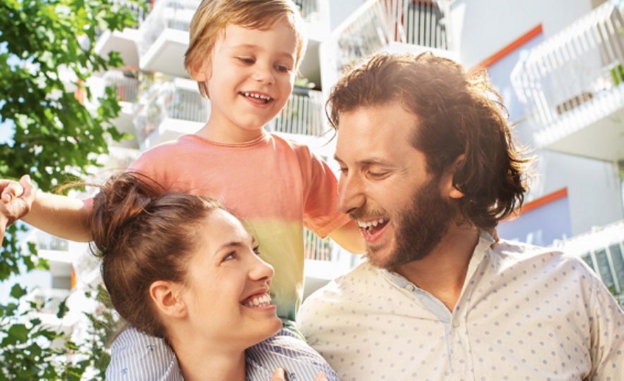 fröhliche Familie steht vor einem Haus mit mehreren Balkonen